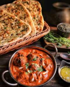 Bowl of orange curry sauce and chicken with naan break on the side