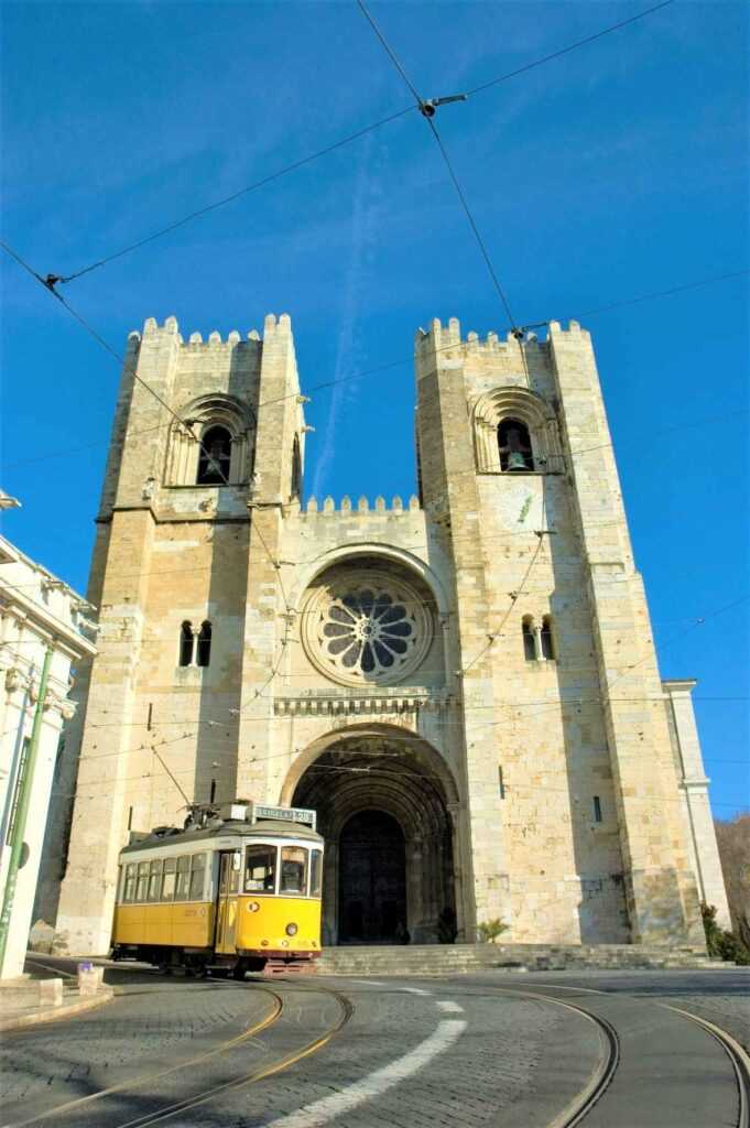 Brown concrete structure with yellow tram passing by during daytime