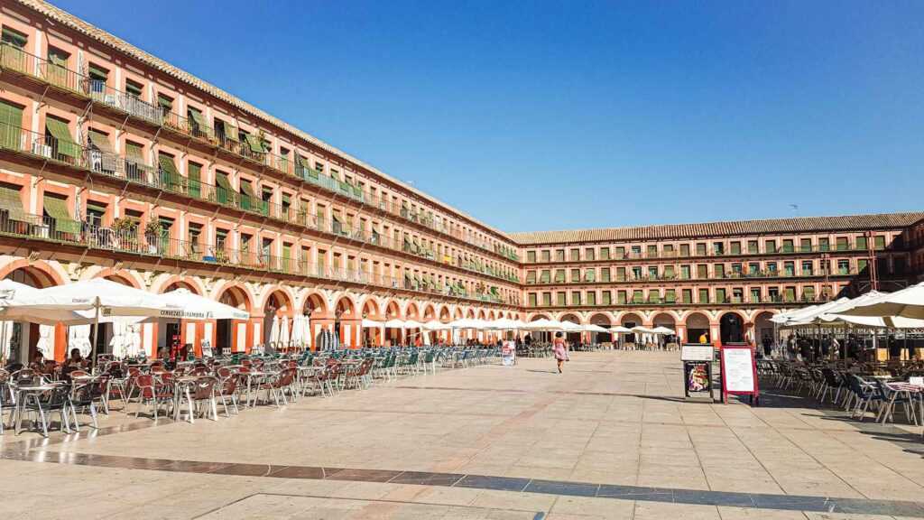 concrete building surrounding a square with tables and chairs places in the courtyard during daytime