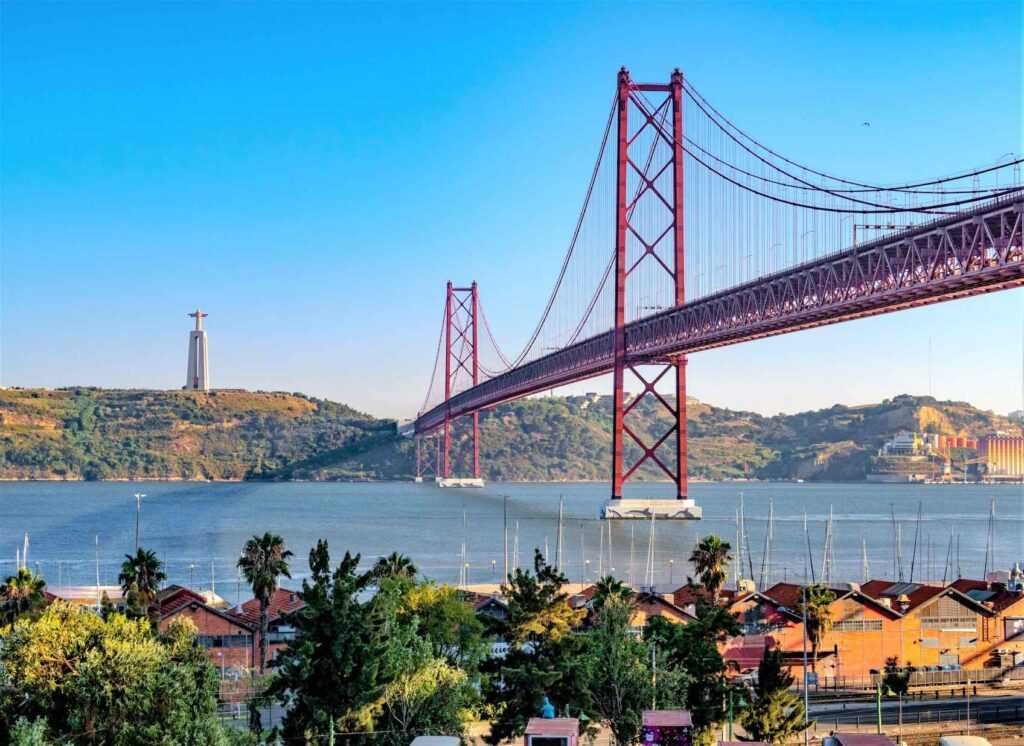 Red suspension bridge over a body of water surrounded by greenery during daytime