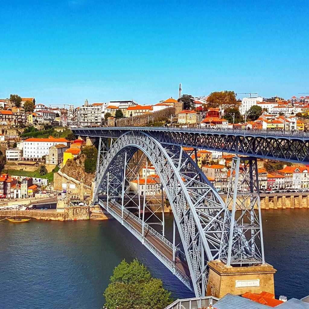 Steel Bridge over a body of water with colorful houses in the background during daytime. One of the most famous landmarks in Portugal