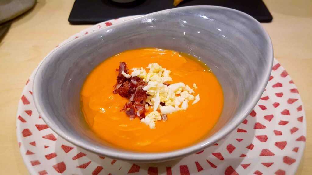 orange soup in a grey bowl topped with crunchy bacon bits and cheese