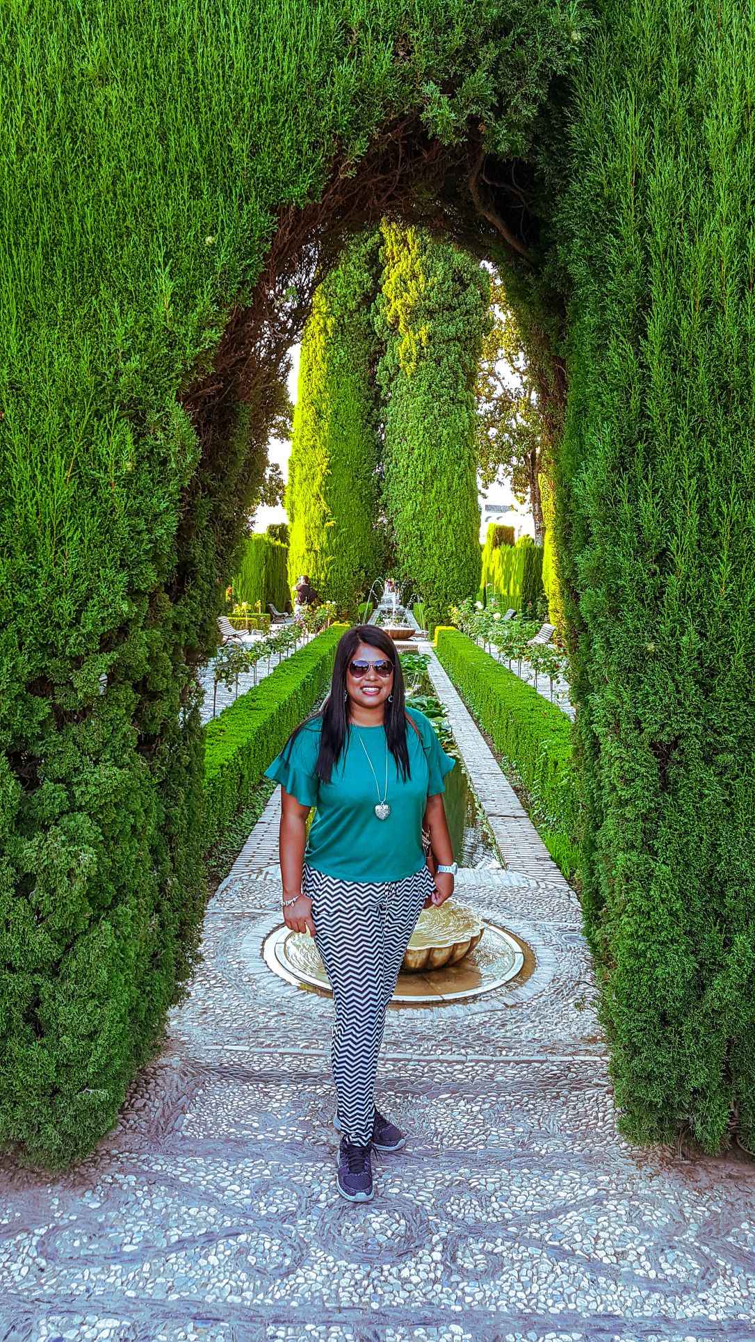 Girl standing in the midst of lush green gardens surrounded with trees all around