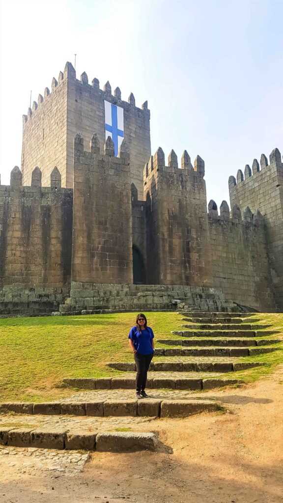 Brown stone castle with green lawns in the front and a girl standing on them during daytime