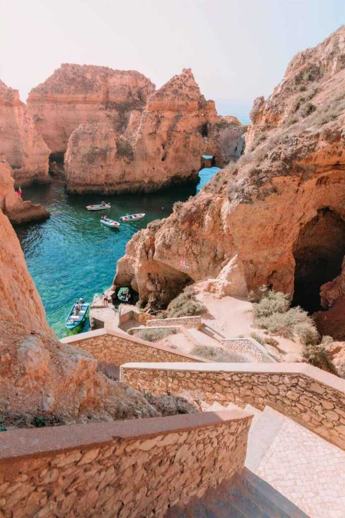 Limestone rocks near turquoise body of water with boats during day time. One of the most famous landmarks in Portugal