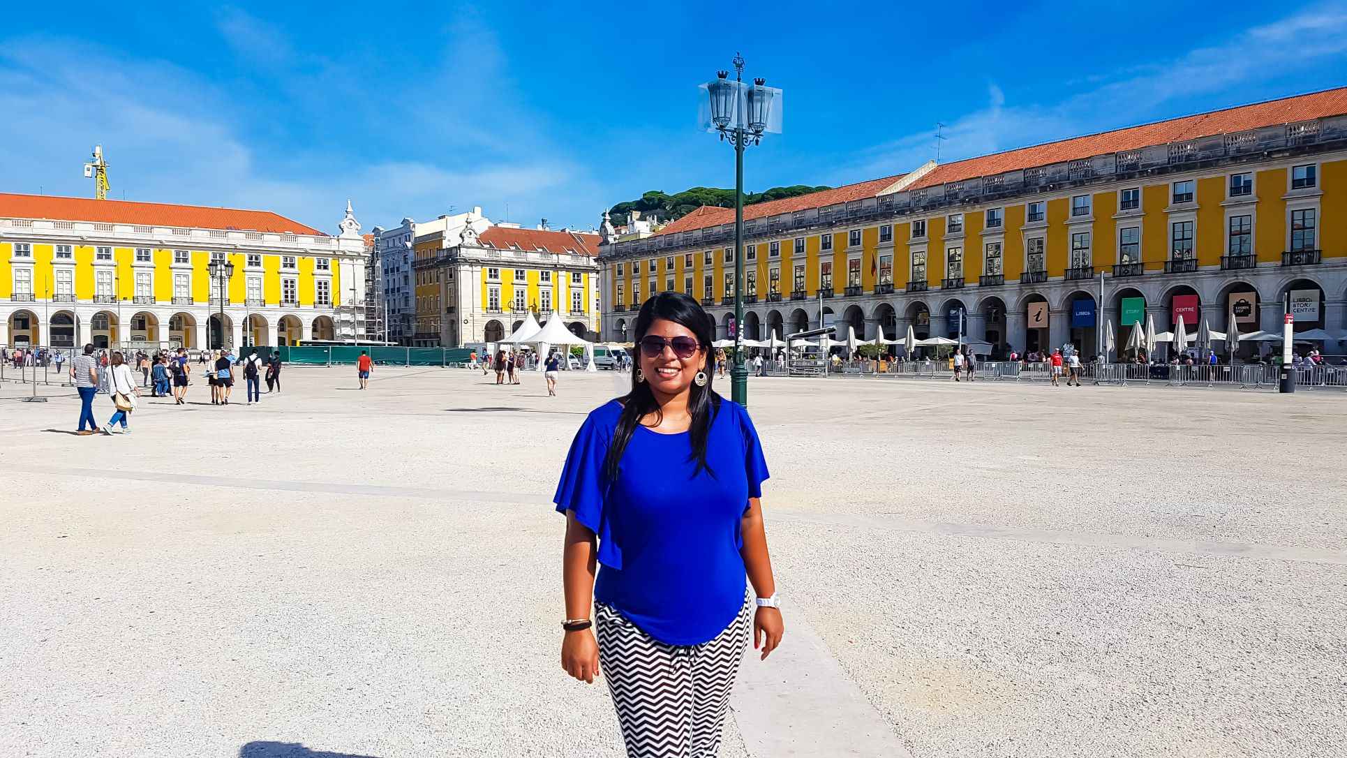 Girl standing in the middle of a large square surrounded by yellow concrete buildings during day time