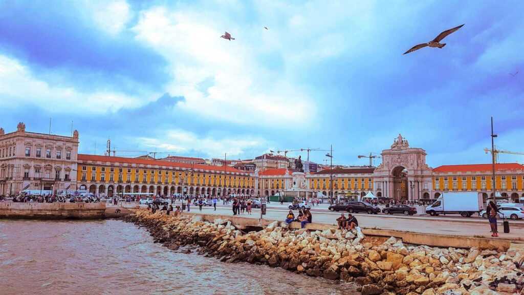 body of water in front of a square surrounded by yellow concrete buildings during daytime. one of the most famous landmarks in Portugal