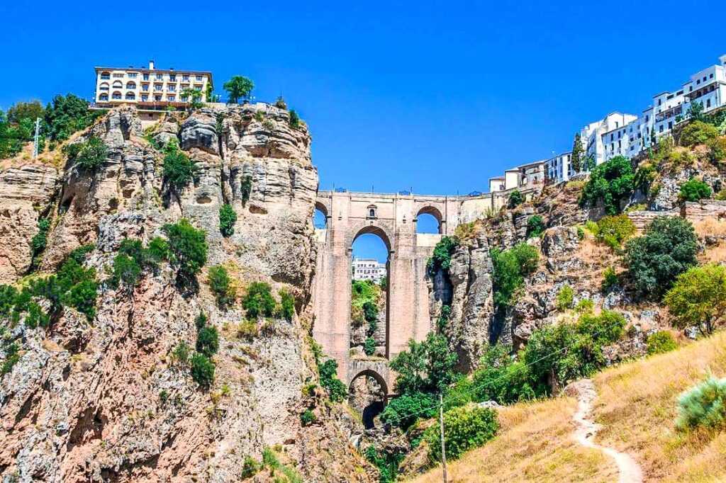 Beige stone bridge near mountains and green trees during daytime. Don't miss this place on your Southern Spain itinerary