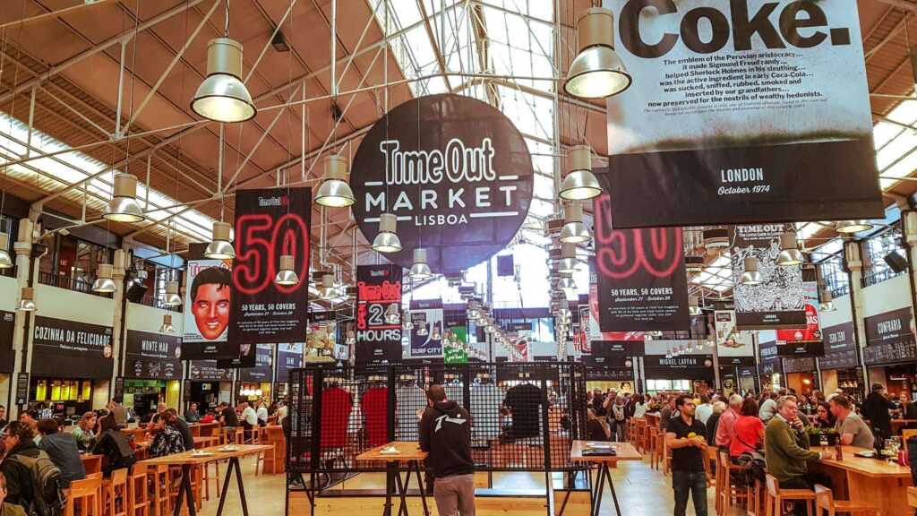 indoor market with stalls, tables and chairs and people all around. one of the best places to visit in Lisbon