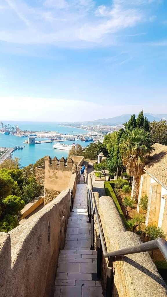 Ariel view of beige castle walls and blue sea in the distance with ships anchored during day time