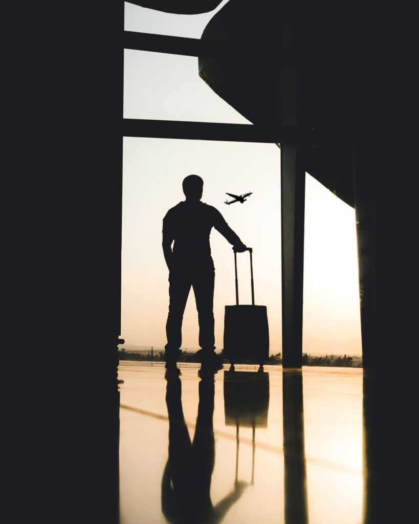 Man Standing near a window with bag during sunset watching a plane take off