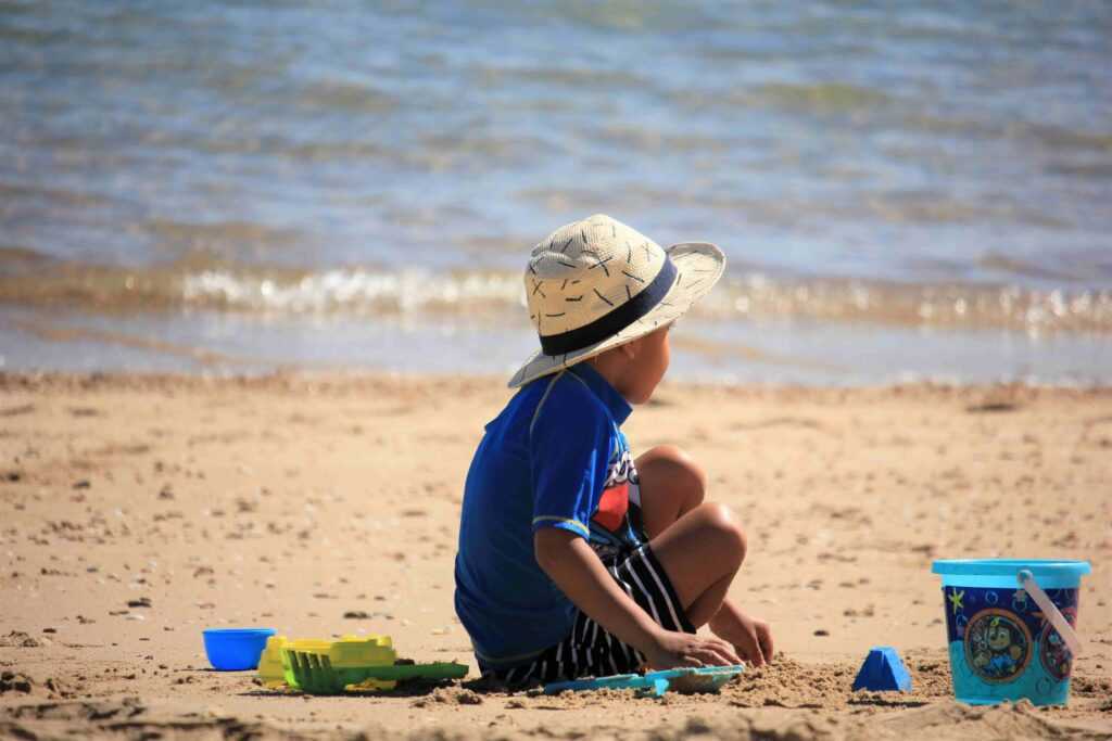 Boy sitting on a beach with toys during daytime