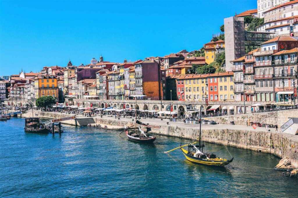 Colorful houses near a river with boats on it during day time. One of the best places to visit in Porto