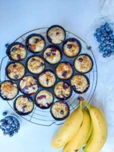 banana blueberry muffins on a tray next to some fresh bananas and blueberries