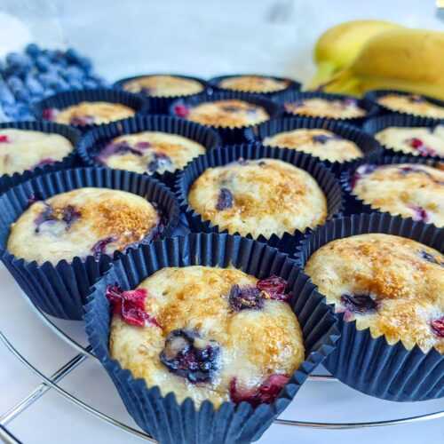 banana blueberry muffins on a tray next to some fresh bananas and blueberries