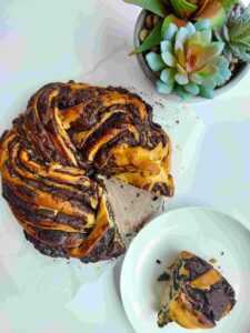 Brown bread with dark chocolate filling on a white table with a slice on a plate and a green plant in the background