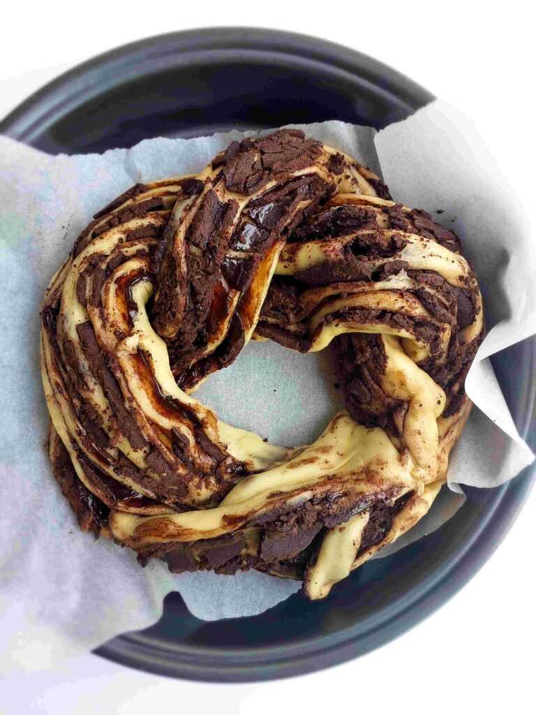 Brown bread dough with dark chocolate filling on a white table with a slice on a plate and a green plant in the background