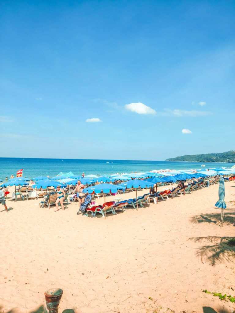 White sandy beach with beach chairs and blue umbrellas on the sand and crystal blue waters in the distance during day time