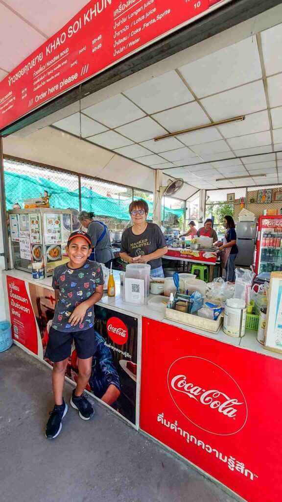 Boy standing infront of counter with lady serving food behind red counter