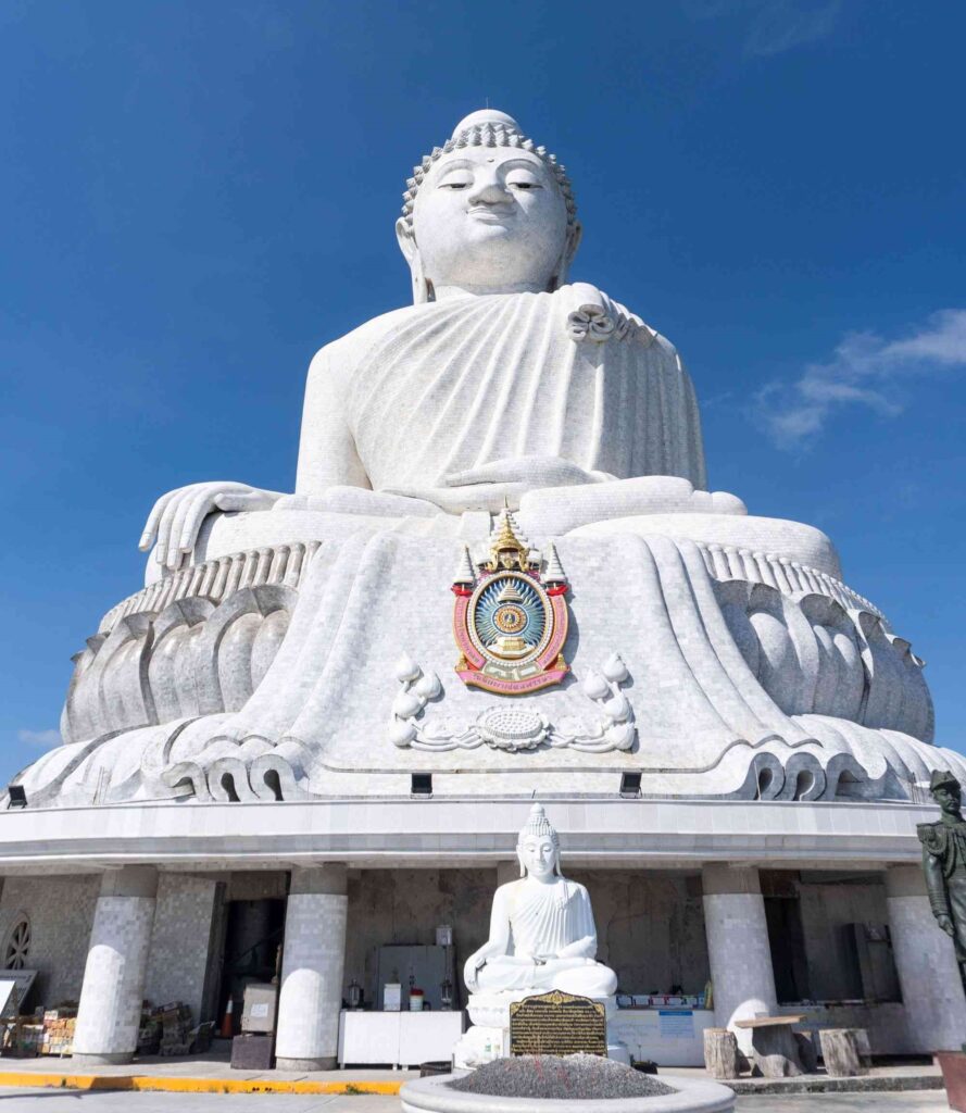 Massive white statue of Big Buddha sitting on top of a hill during day time