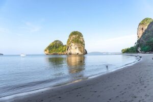 brown sand near water with limestone cliff in the distance during sunrise