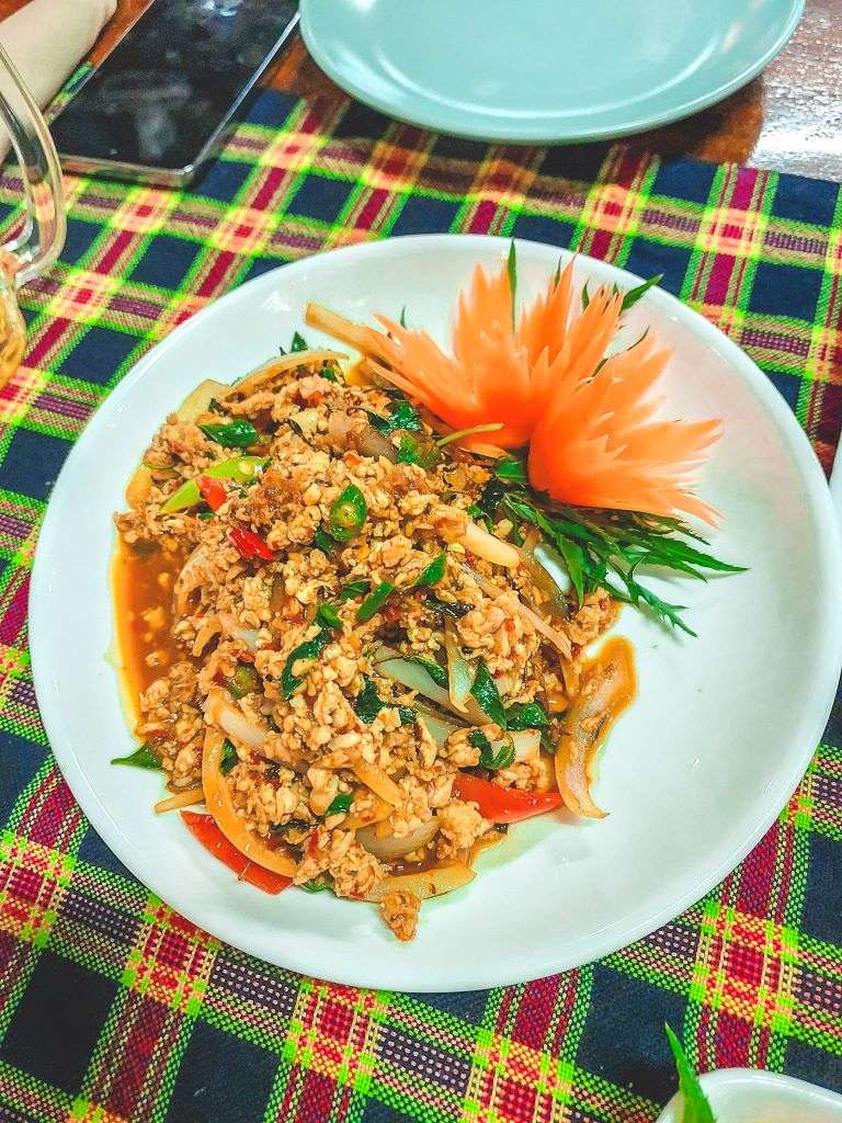 Stir fried pork mince with green Thai Basil leaves and an orange garnish on the side