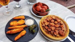 golden chicken tenders on a black plate, chopped pieces of octopus on a wooden plate and meatballs covered in a red tomato sauce in a ramekin