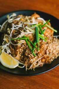 a plate of noodles with a lemon wedge served on a black plate on a wooden table