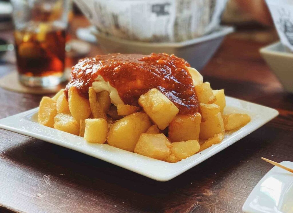 golden fried chunks of potato topped with a red tomato based sauce on a white plate