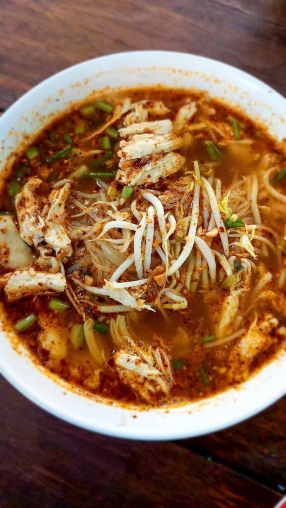 white bowl with brown soup and chicken topped with white sprouts