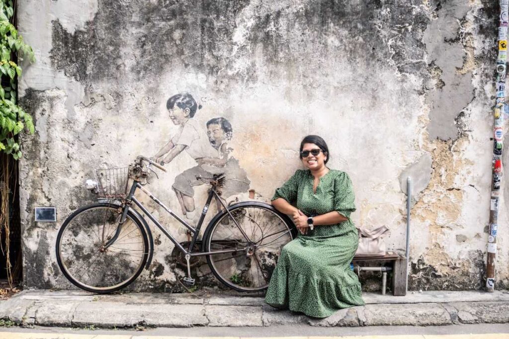 Girl sitting next to art of bike with two kids on it