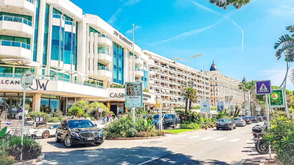 Hotel buildings lined on side of street with luxury cars parked all over the street.